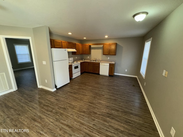 kitchen with dark wood-type flooring, a sink, white appliances, under cabinet range hood, and baseboards