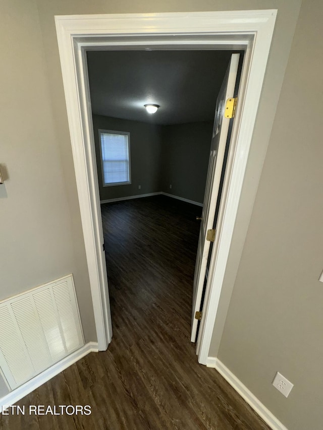 hallway with dark wood-type flooring, visible vents, and baseboards