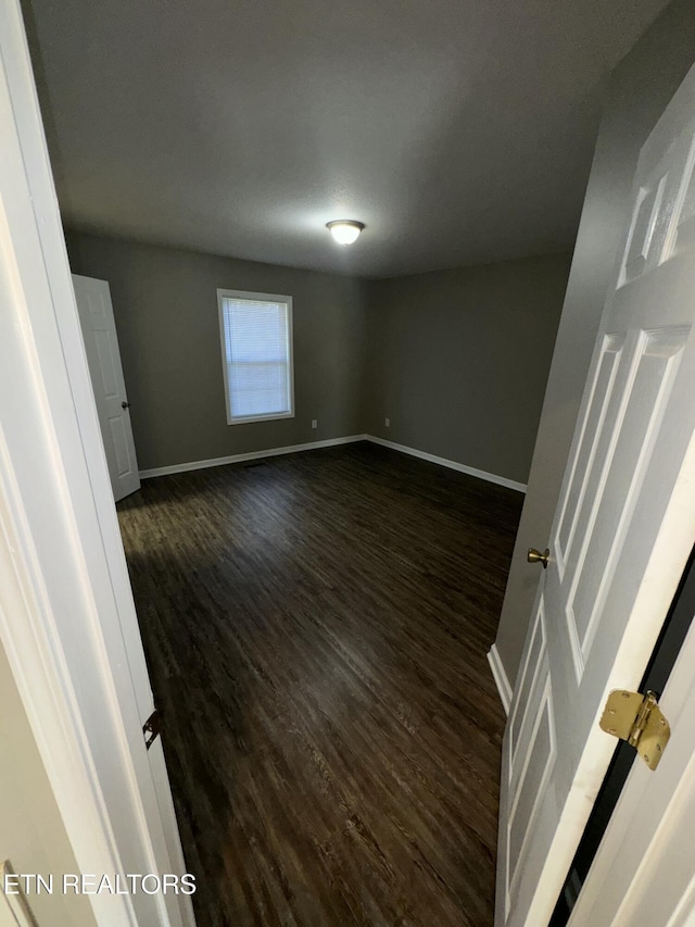 empty room featuring dark wood-type flooring and baseboards