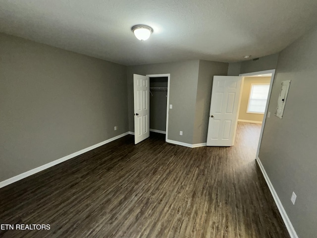 unfurnished bedroom featuring a textured ceiling, a closet, baseboards, and dark wood-type flooring