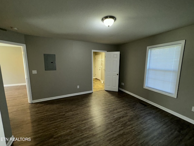 empty room featuring a textured ceiling, electric panel, baseboards, and dark wood-type flooring