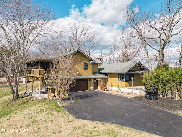 view of front of house with stairway, a front yard, a garage, a sunroom, and driveway