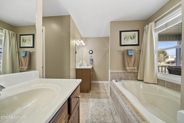 bathroom featuring a sink, two vanities, a bath, and tile patterned floors