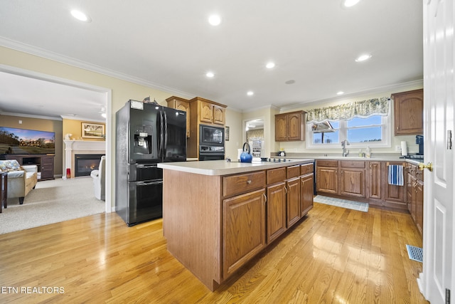 kitchen featuring visible vents, a kitchen island with sink, ornamental molding, black appliances, and a glass covered fireplace