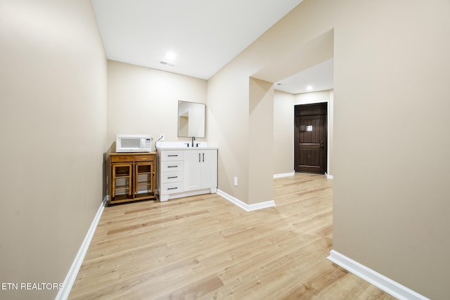 bar with a sink, light wood-style floors, baseboards, and white microwave