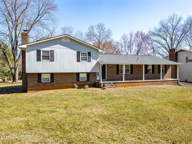 tri-level home featuring brick siding, covered porch, a chimney, and a front yard