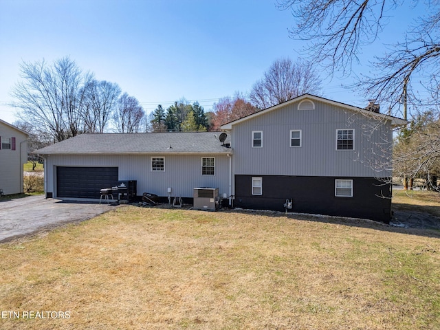 rear view of property featuring central AC, an attached garage, a lawn, and driveway