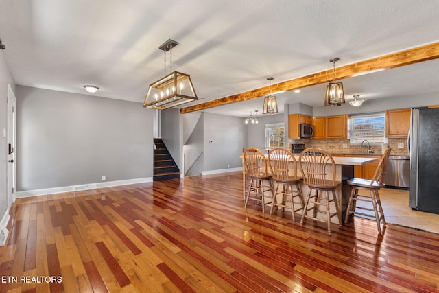 kitchen with baseboards, decorative backsplash, light wood-style floors, appliances with stainless steel finishes, and a kitchen breakfast bar