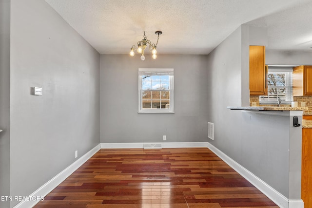 unfurnished dining area featuring hardwood / wood-style floors, baseboards, visible vents, a textured ceiling, and a notable chandelier