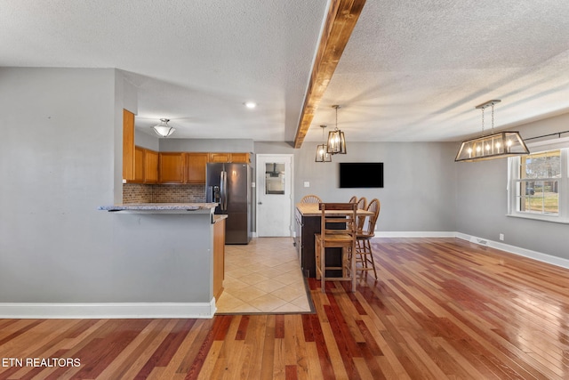 kitchen featuring brown cabinets, light wood-style flooring, stainless steel refrigerator with ice dispenser, a peninsula, and decorative backsplash