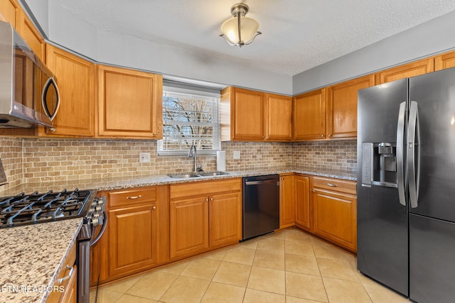 kitchen featuring light tile patterned floors, stainless steel appliances, brown cabinetry, and a sink