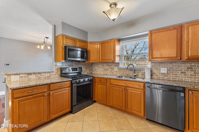 kitchen with stone counters, brown cabinets, stainless steel appliances, and a sink