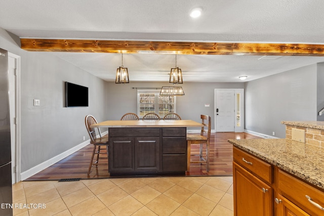 kitchen featuring light tile patterned floors, beamed ceiling, a breakfast bar area, and baseboards