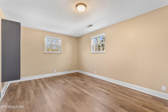 spare room featuring visible vents, a textured ceiling, baseboards, and wood finished floors