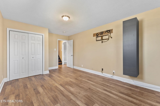 unfurnished bedroom with a textured ceiling, wood finished floors, a closet, arched walkways, and baseboards