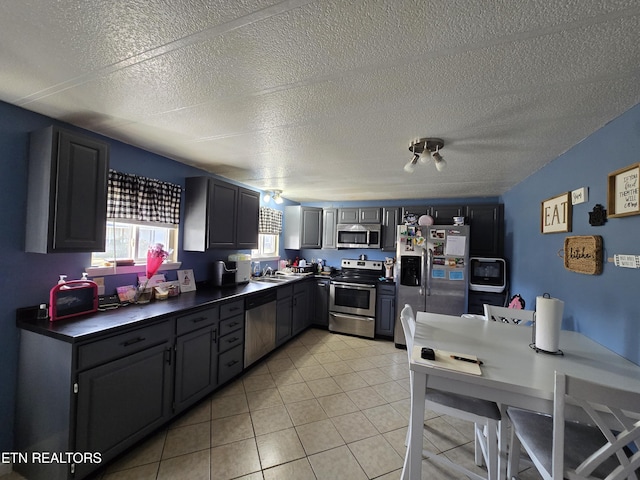 kitchen with light tile patterned floors, a textured ceiling, a sink, appliances with stainless steel finishes, and dark countertops