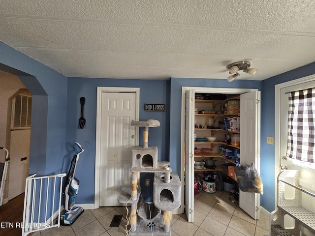 interior space featuring arched walkways, visible vents, a textured ceiling, tile patterned flooring, and baseboards