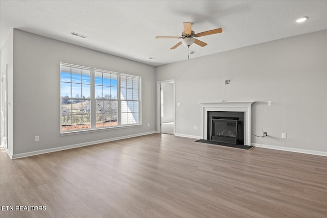 unfurnished living room with wood finished floors, a glass covered fireplace, and baseboards