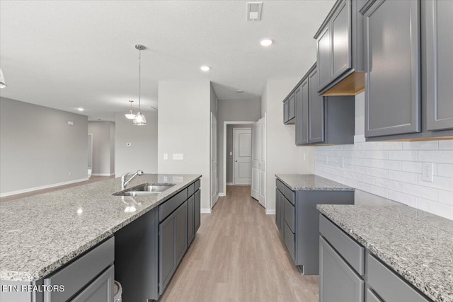 kitchen with light stone counters, light wood finished floors, tasteful backsplash, visible vents, and a sink