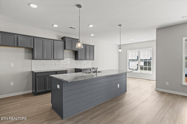 kitchen featuring visible vents, decorative backsplash, a sink, and wood finished floors