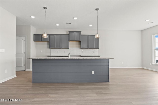 kitchen with visible vents, light wood-style flooring, decorative backsplash, a kitchen island with sink, and baseboards