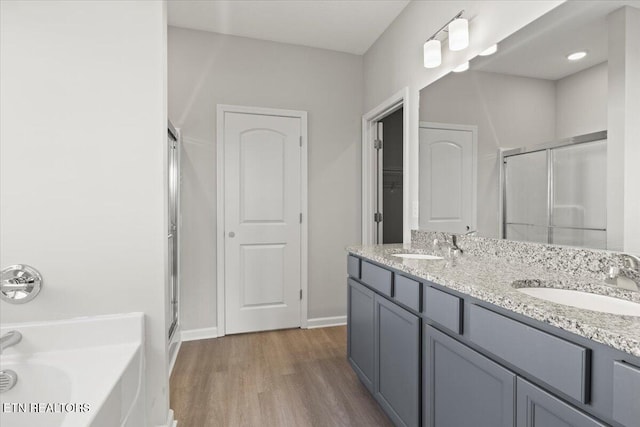 bathroom with a stall shower, a sink, a bath, and wood finished floors