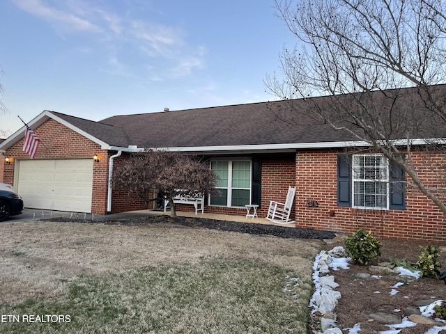 ranch-style home featuring an attached garage, brick siding, a front lawn, and a shingled roof