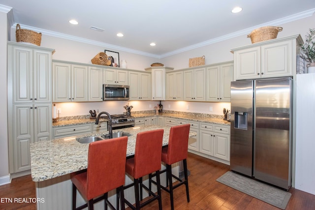 kitchen with stainless steel appliances, dark wood-type flooring, ornamental molding, a sink, and an island with sink