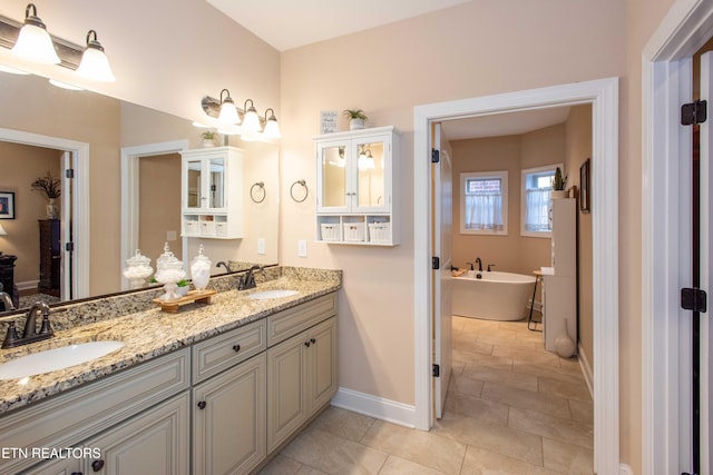 full bath with baseboards, a sink, a freestanding bath, and double vanity