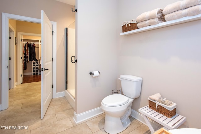 bathroom with tile patterned flooring, a shower stall, toilet, and a walk in closet