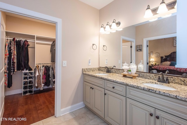 ensuite bathroom with double vanity, ensuite bath, a sink, and baseboards