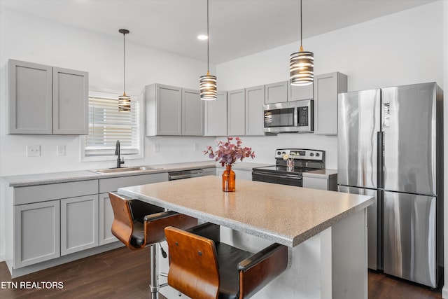 kitchen featuring stainless steel appliances, a sink, a center island, and gray cabinetry