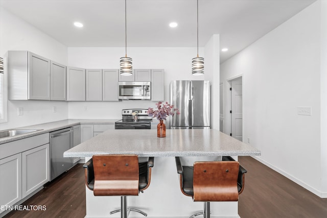 kitchen featuring a breakfast bar area, appliances with stainless steel finishes, dark wood-style flooring, a center island, and gray cabinets