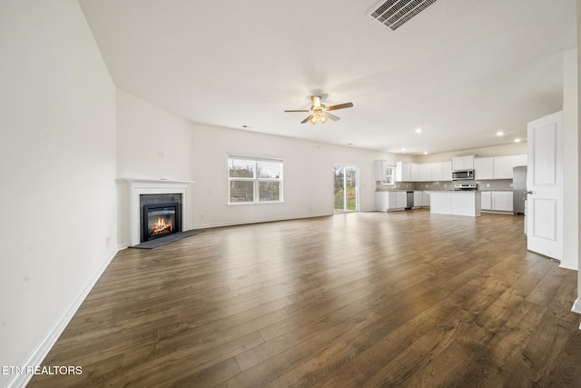 unfurnished living room featuring dark wood-style floors, visible vents, a ceiling fan, a glass covered fireplace, and baseboards