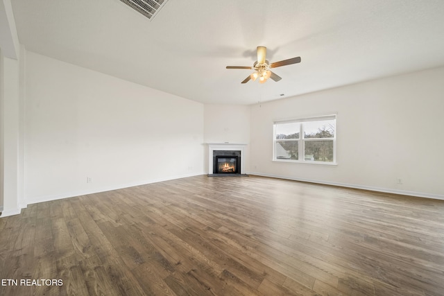 unfurnished living room with visible vents, a glass covered fireplace, ceiling fan, wood finished floors, and baseboards