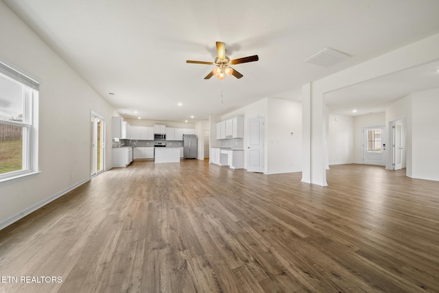 unfurnished living room with a ceiling fan, a wealth of natural light, visible vents, and wood finished floors