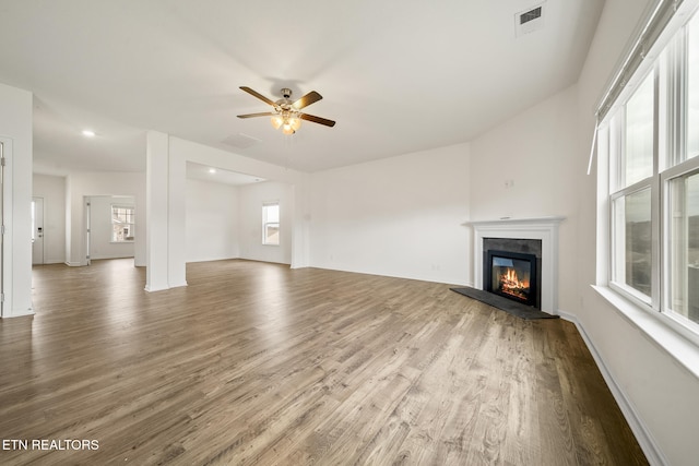 unfurnished living room with visible vents, a ceiling fan, a glass covered fireplace, wood finished floors, and baseboards