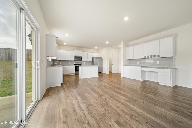 kitchen with light wood finished floors, white cabinetry, stainless steel appliances, and decorative backsplash