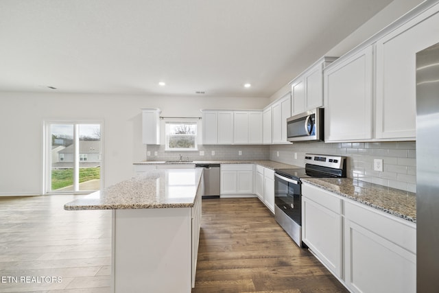 kitchen featuring dark wood-style floors, a center island, stainless steel appliances, tasteful backsplash, and a sink