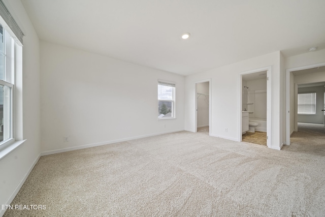 unfurnished bedroom with baseboards, ensuite bathroom, a walk in closet, carpet floors, and a closet