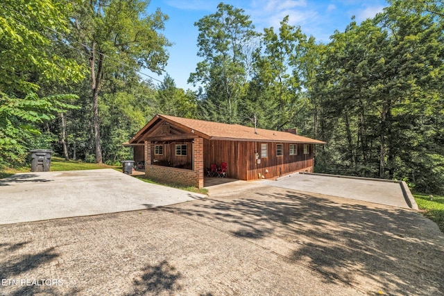 exterior space featuring board and batten siding, concrete driveway, a chimney, and a forest view