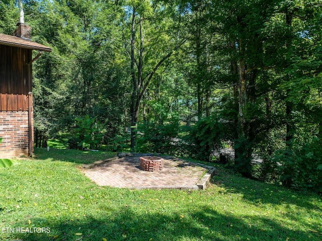 view of yard featuring a forest view, an outdoor fire pit, and a patio