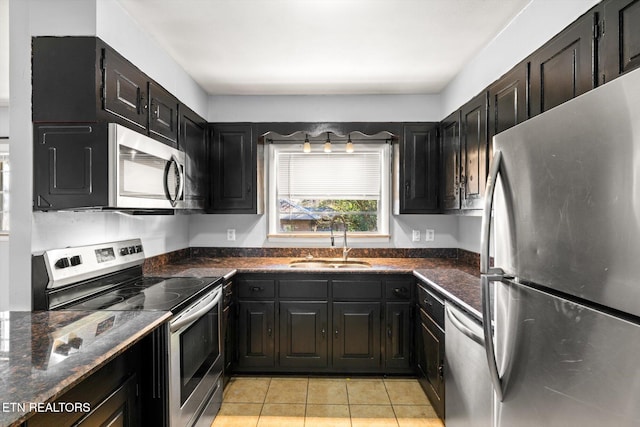 kitchen featuring light tile patterned floors, dark cabinets, a sink, appliances with stainless steel finishes, and dark stone countertops