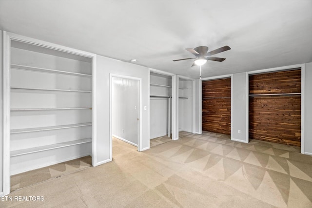 unfurnished bedroom with light carpet, wood walls, baseboards, and two closets