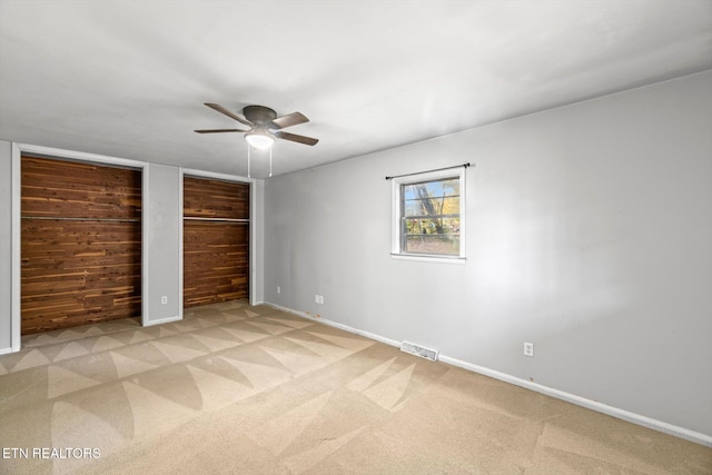 unfurnished bedroom with light carpet, baseboards, and multiple closets