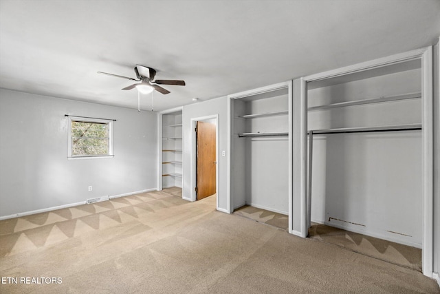 unfurnished bedroom with multiple closets, light colored carpet, visible vents, a ceiling fan, and baseboards