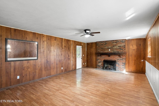 unfurnished living room with ceiling fan, light wood-style flooring, wood walls, a fireplace, and baseboards