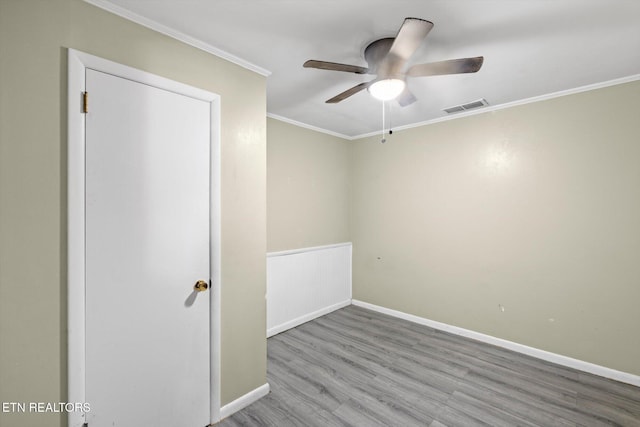 spare room with wood finished floors, visible vents, baseboards, a ceiling fan, and ornamental molding