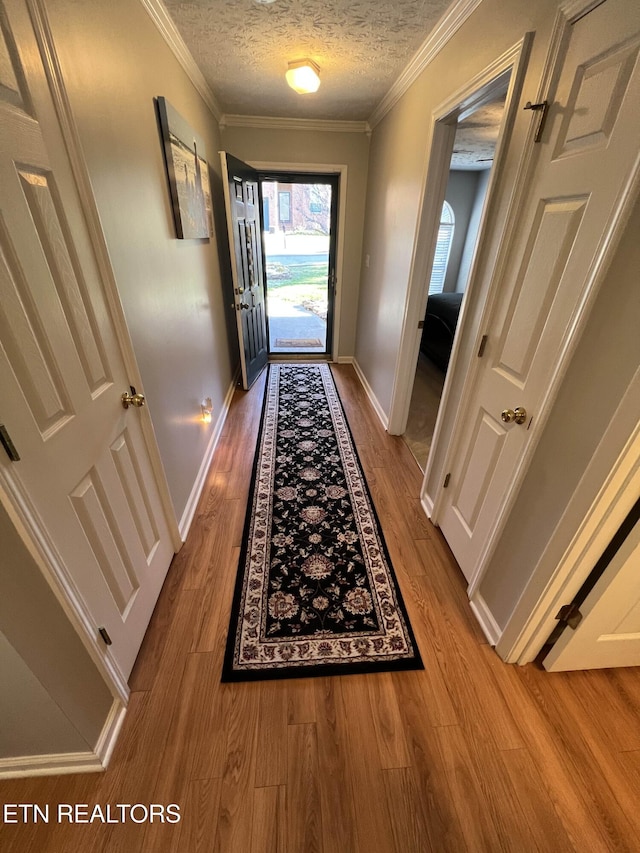 entryway featuring a textured ceiling, ornamental molding, wood finished floors, and baseboards