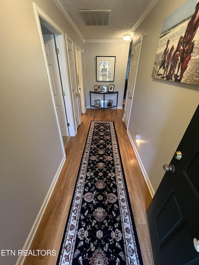 hall featuring a textured ceiling, visible vents, wood finished floors, and ornamental molding